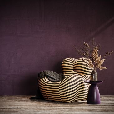 Striped, curvy armchair beside a purple side table with dried flowers.